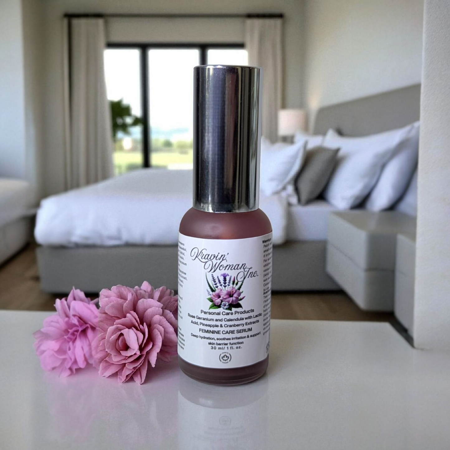 Premium handmade feminine care serum by Kravin Woman Inc—pineapple and cranberry natural formula in a luxury frosted glass bottle; eco-friendly and female-owned in Calgary, Canada. Serum bottle with pink flowers on a table in a bedroom setting