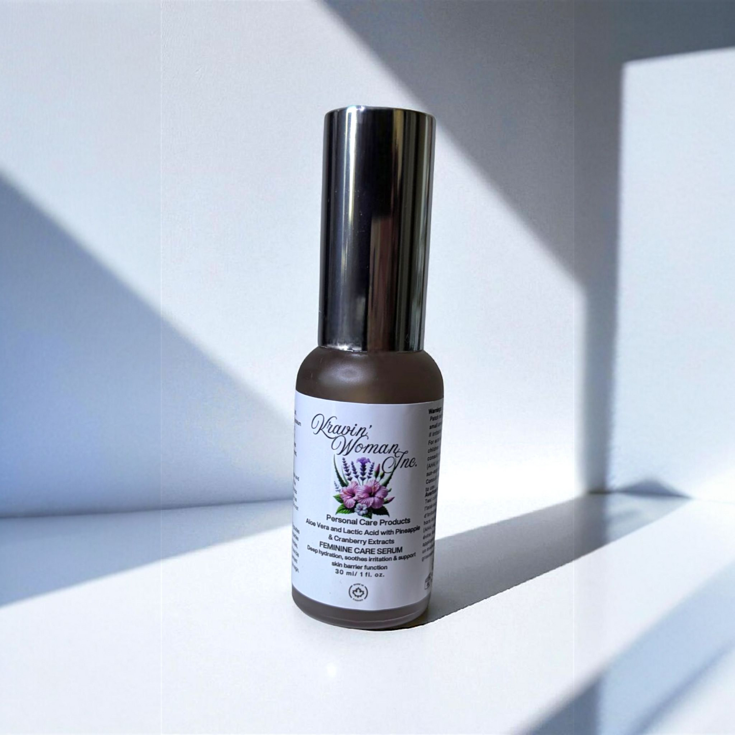 Eco-friendly luxury feminine serum from Kravin Woman Inc—aloe, lactic acid, pineapple, and cranberry infused formula; handmade by a female-owned Calgary skincare brand. frosted glass pump bottle on white countertop with cast shadows. 