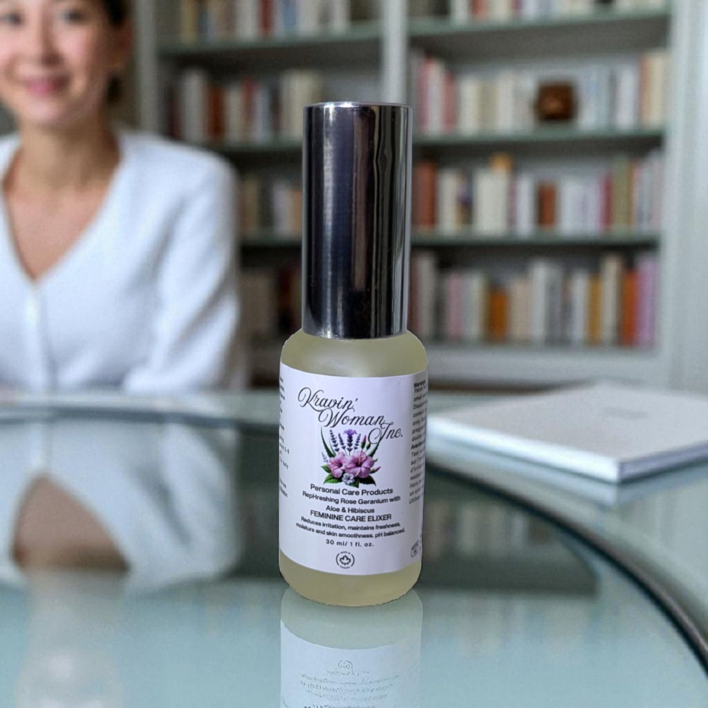 Kravin Woman Inc luxury feminine elixir—rose, aloe, hibiscus, apple cider vinegar, and honey intimate care blend; natural, handcrafted, woman-owned Calgary skincare. Bottle of Kravin Woman Inc on a glass surface with a blurred background of books and a person.